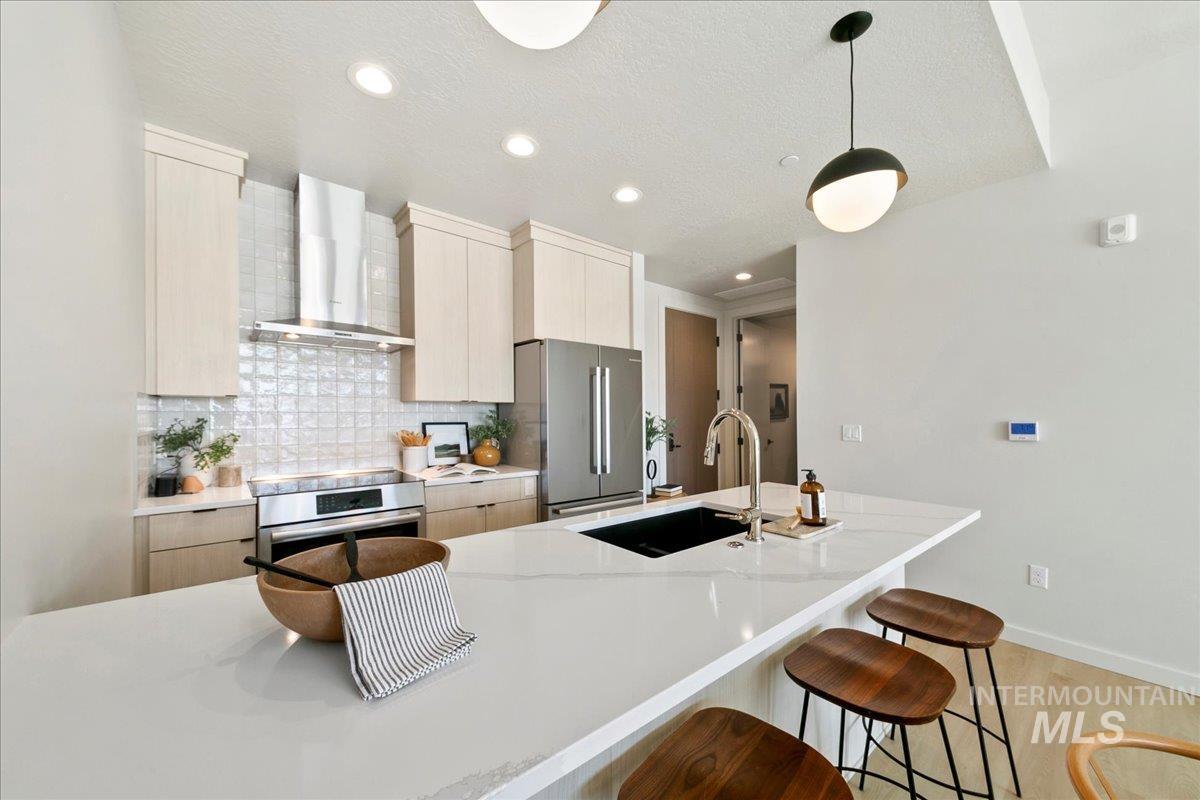 Kitchen with wall chimney exhaust hood, modern cabinets, backsplash, light stone countertops, and a breakfast bar