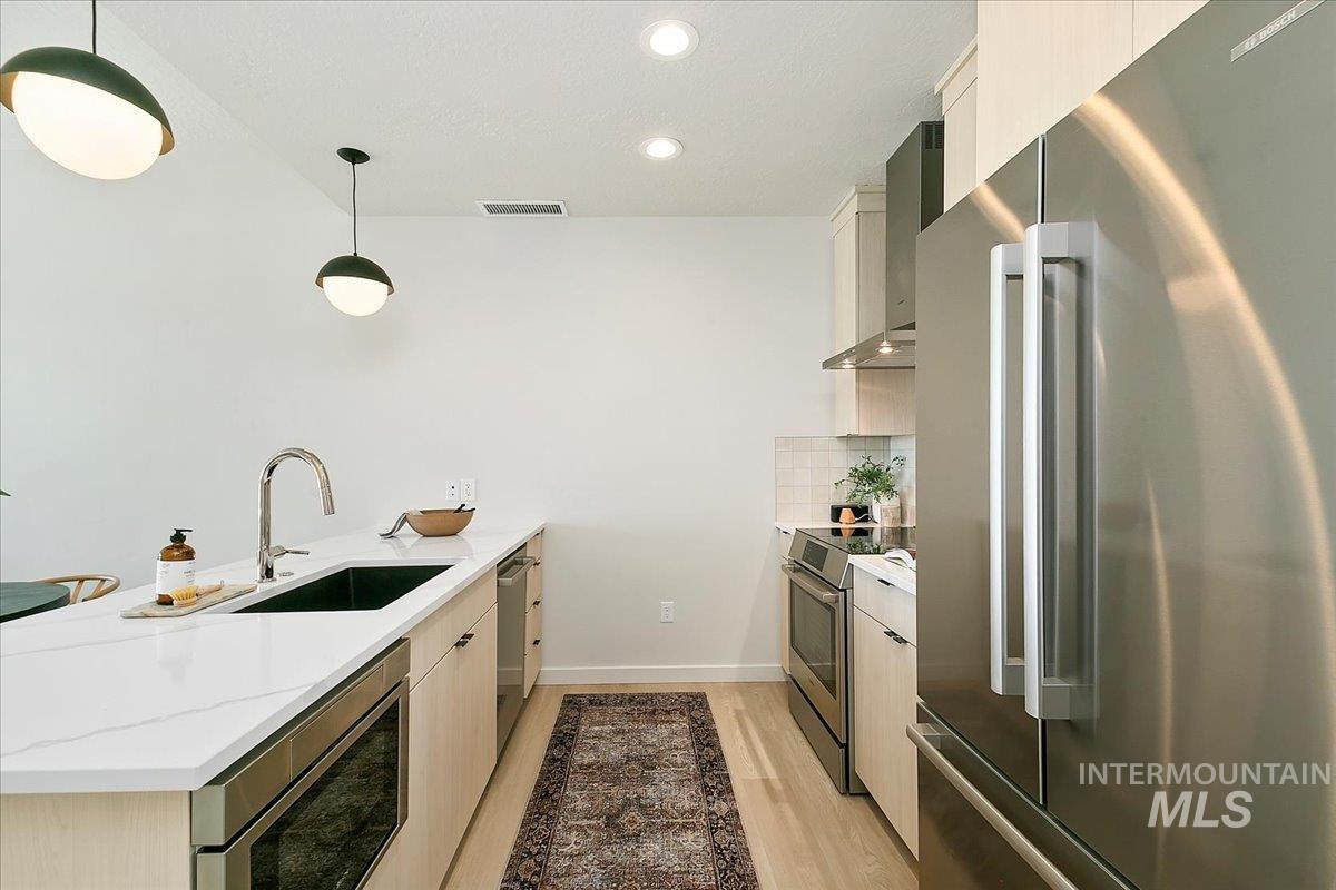 Kitchen featuring appliances with stainless steel finishes, a peninsula, hanging light fixtures, recessed lighting, and light stone counters