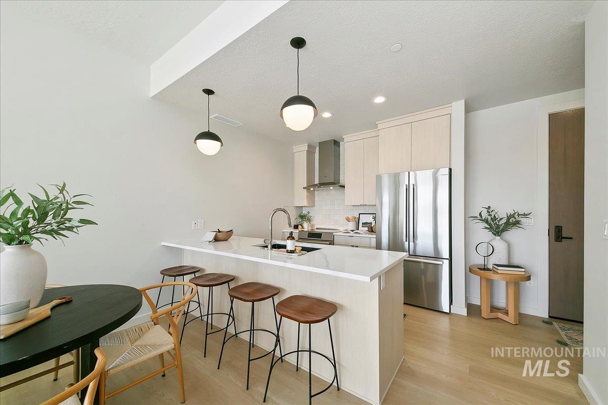 Kitchen featuring freestanding refrigerator, a peninsula, modern cabinets, a breakfast bar, and wall chimney range hood