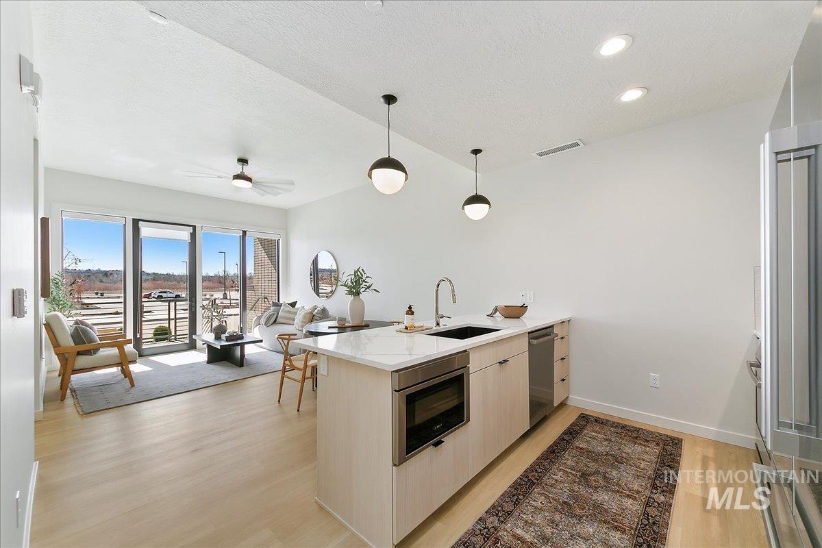 Kitchen featuring a peninsula, modern cabinets, light stone counters, light wood-style floors, and a textured ceiling