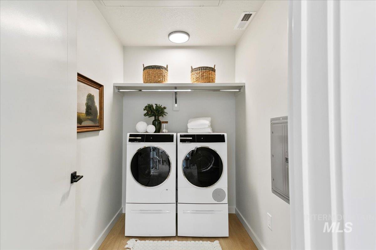 Washroom featuring electric panel, light wood-style flooring, and independent washer and dryer
