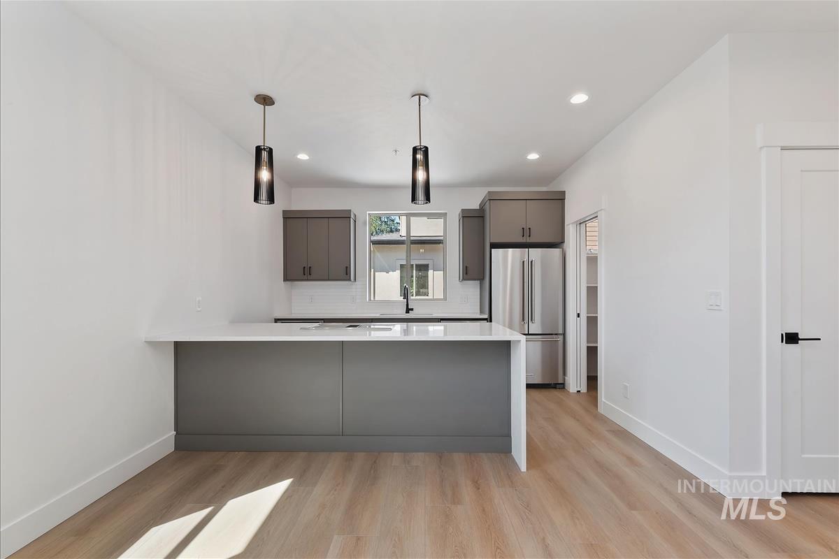 Kitchen with a peninsula, tasteful backsplash, high end refrigerator, gray cabinetry, and light wood-style floors