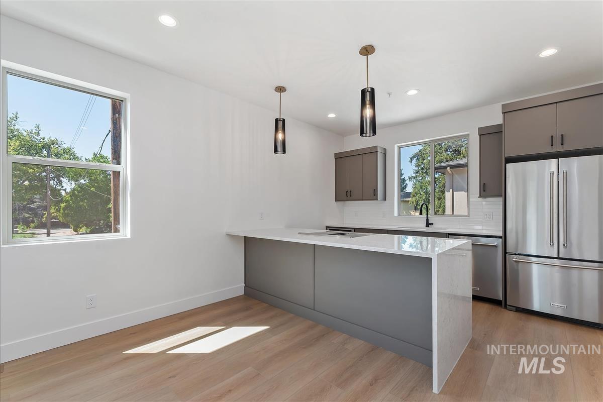 Kitchen with gray cabinetry, stainless steel appliances, a peninsula, hanging light fixtures, and light wood-type flooring