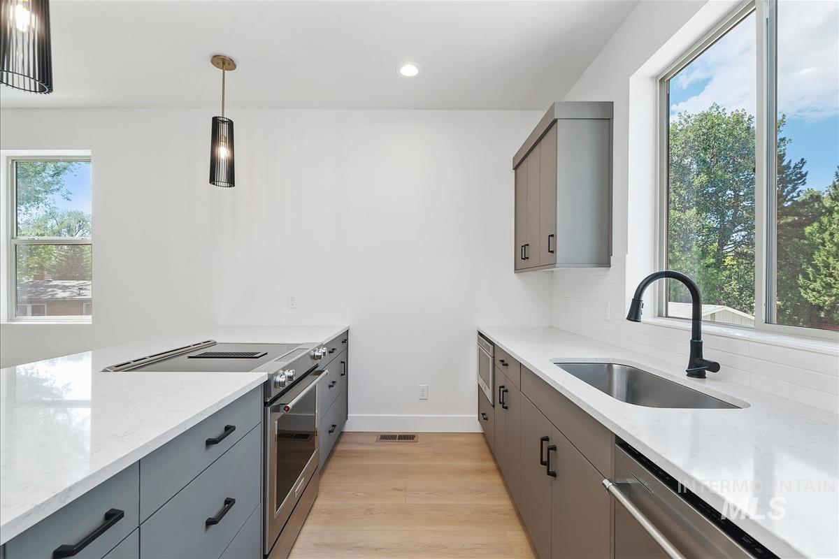 Kitchen with gray cabinetry, appliances with stainless steel finishes, healthy amount of natural light, decorative light fixtures, and recessed lighting
