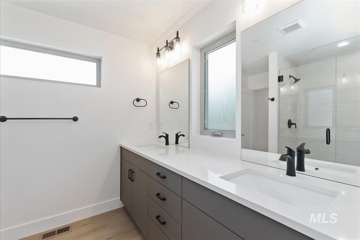 Full bath featuring double vanity, a shower stall, and light wood-style floors