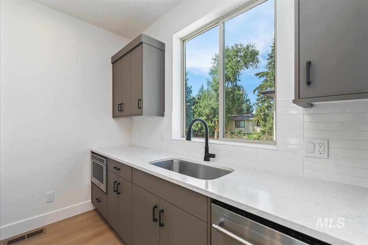 Kitchen featuring gray cabinetry, light stone countertops, tasteful backsplash, and light wood-style floors