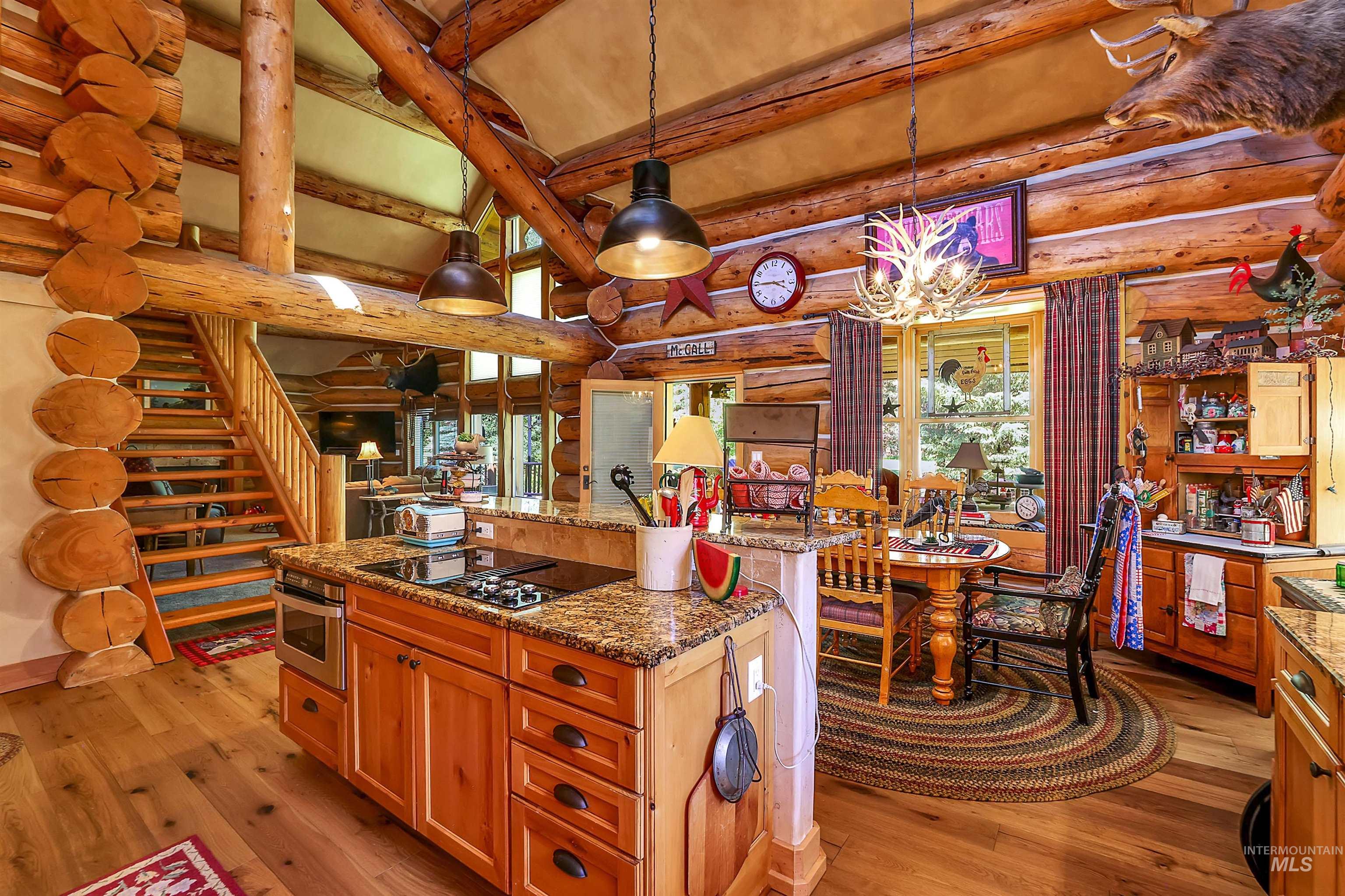 Kitchen featuring log walls, stovetop with downdraft, light wood finished floors, oven, and a chandelier