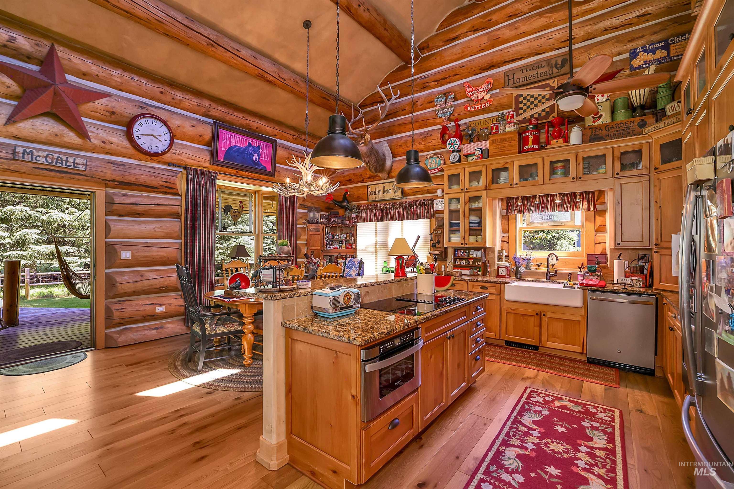 Kitchen with stainless steel appliances, log walls, light wood finished floors, beam ceiling, and stone counters