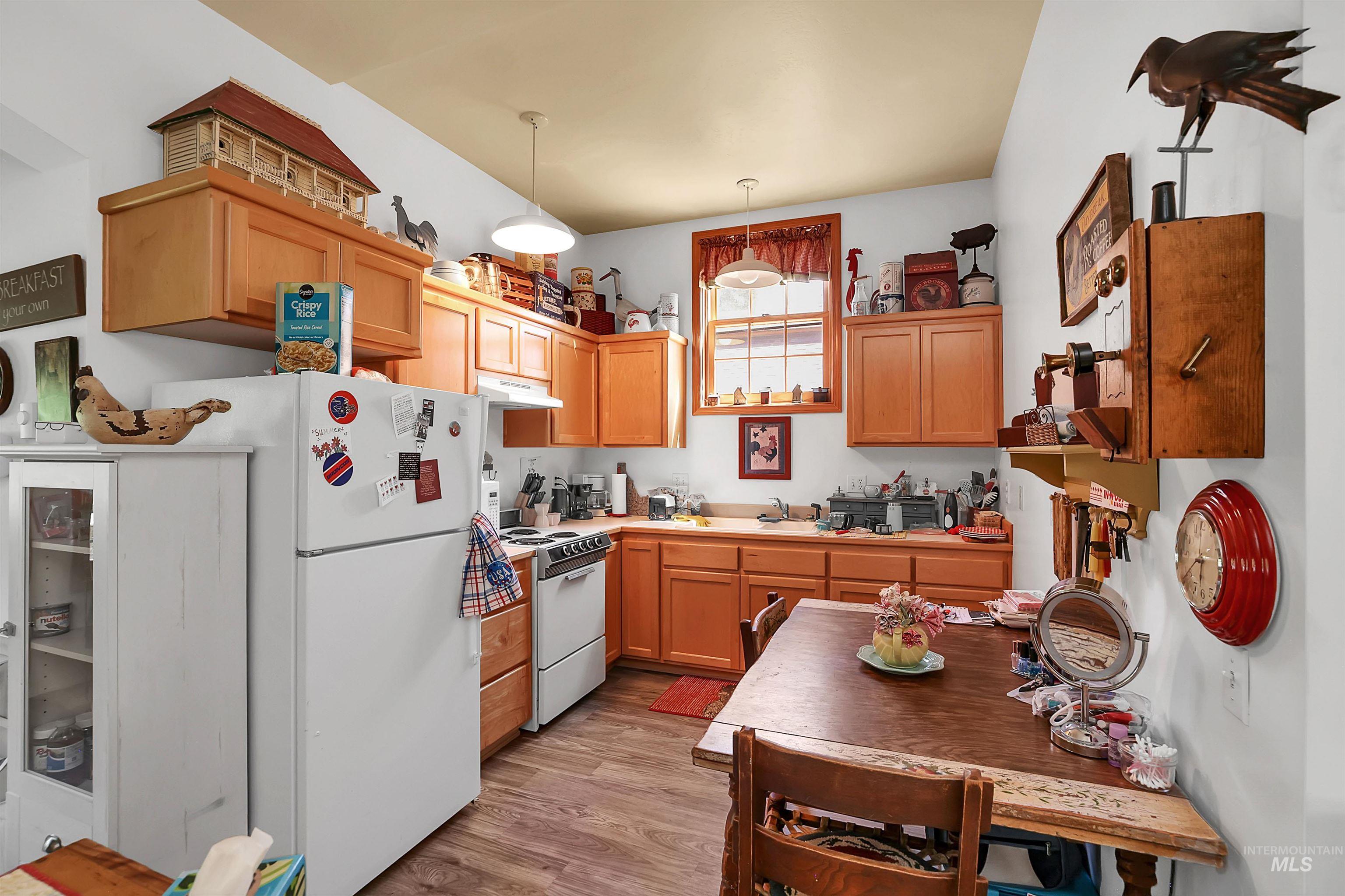 Kitchen featuring white appliances, under cabinet range hood, light wood-style flooring, light countertops, and decorative light fixtures