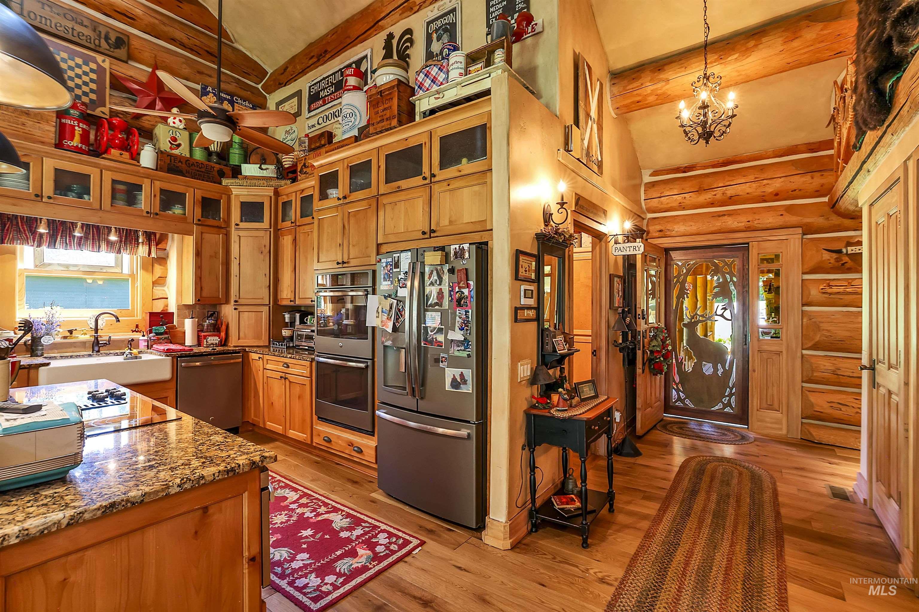 Kitchen featuring stainless steel appliances, rustic walls, light wood-style floors, beam ceiling, and pendant lighting