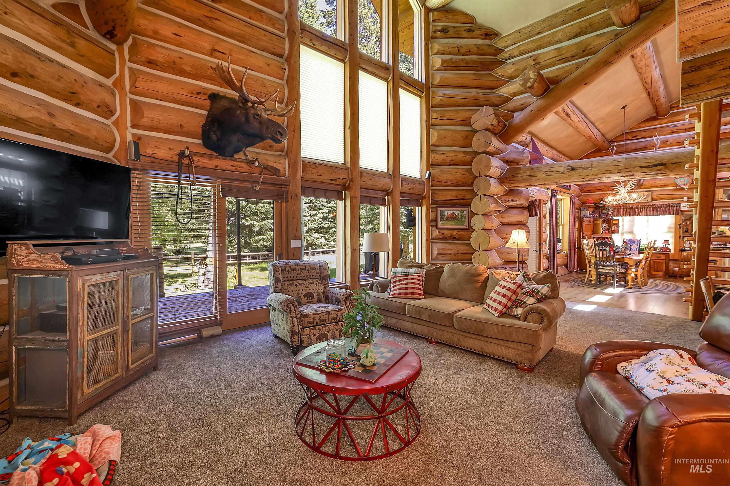 Living room with high vaulted ceiling, carpet floors, rustic walls, plenty of natural light, and beamed ceiling
