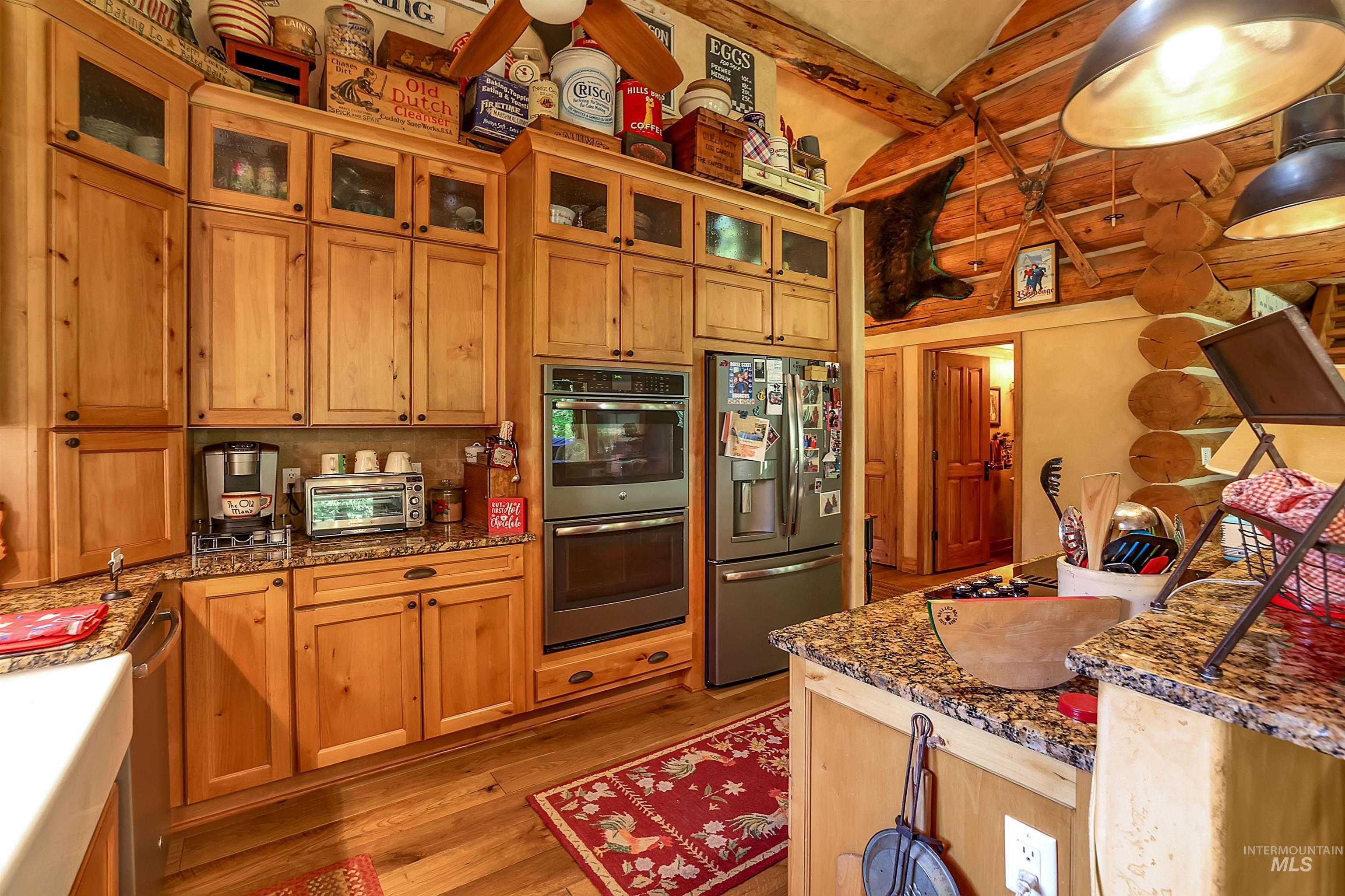 Kitchen with stainless steel appliances, light wood finished floors, dark stone counters, glass insert cabinets, and high vaulted ceiling