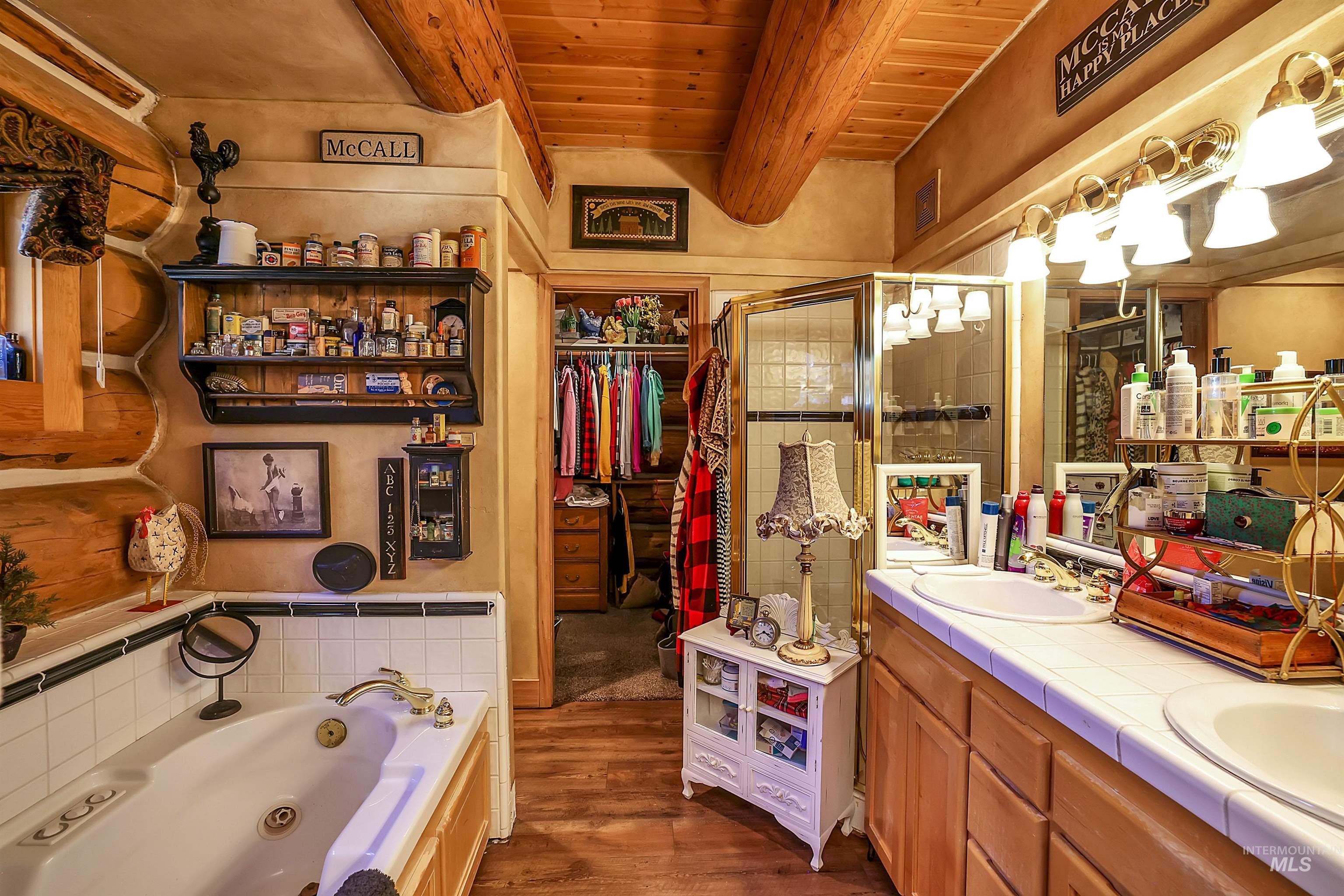 Full bath featuring a wood ceiling with exposed beams, wood finished floors, double vanity, a jetted tub, and a shower stall