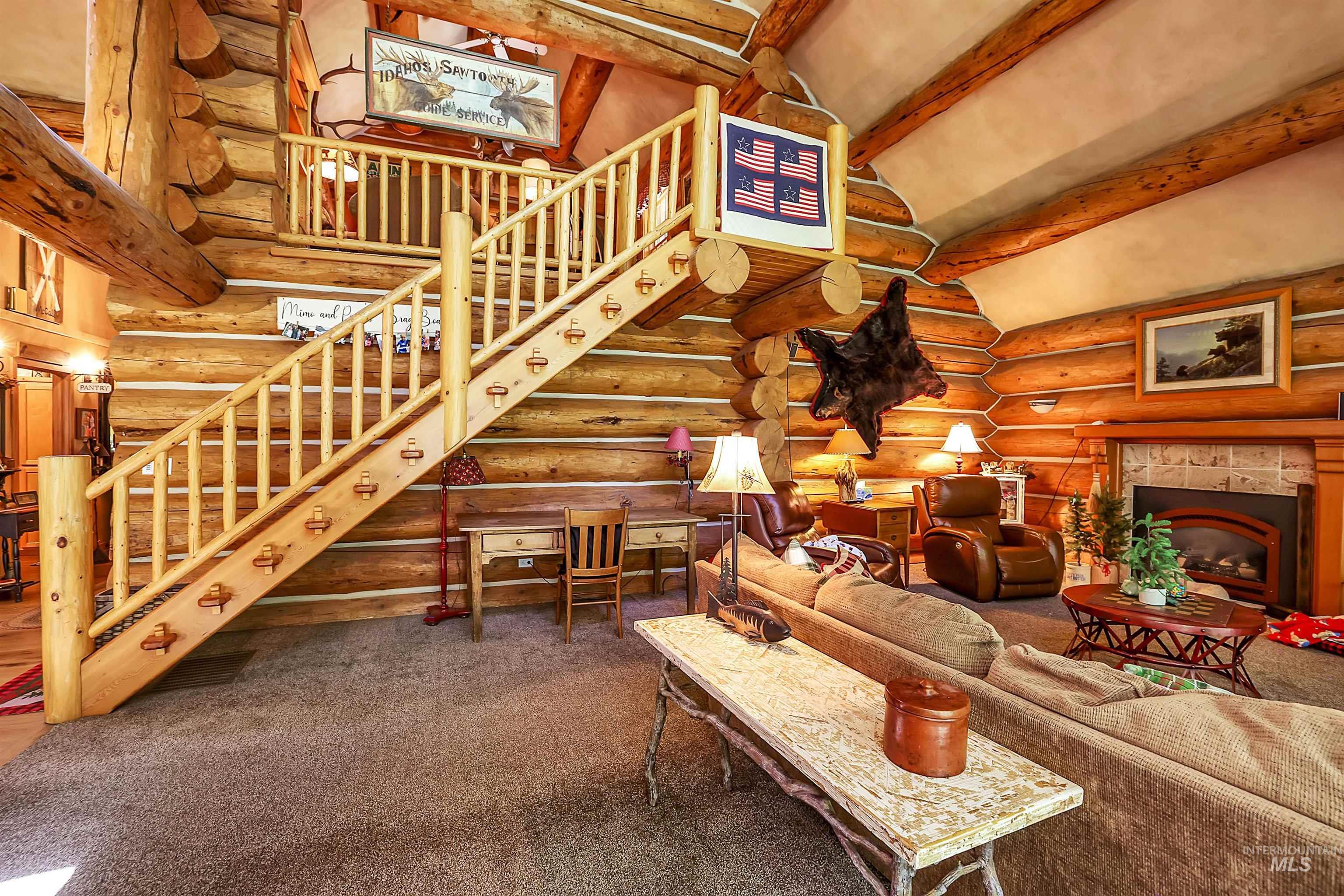 Carpeted living area featuring rustic walls, stairs, a tile fireplace, high vaulted ceiling, and beamed ceiling