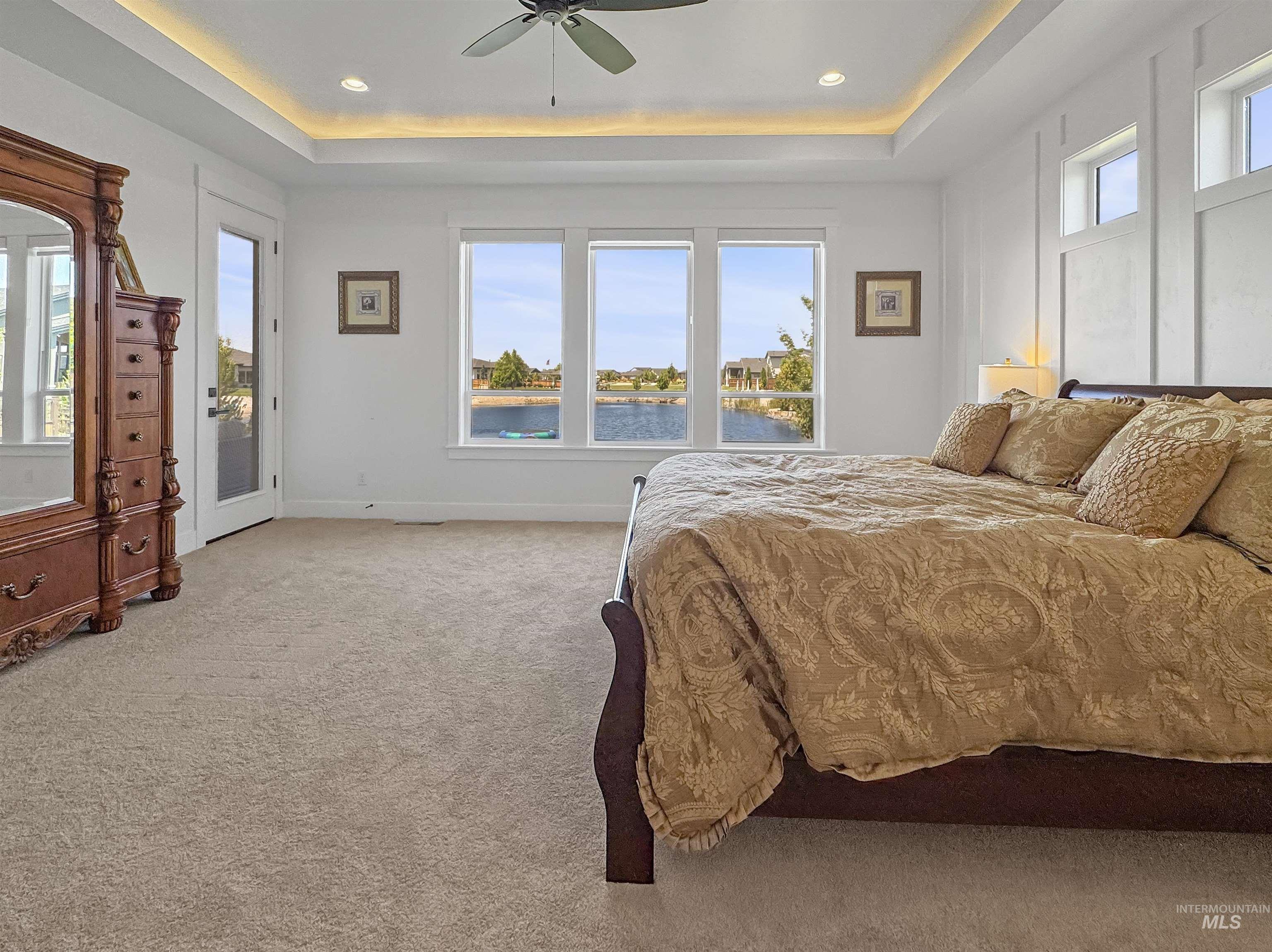Carpeted bedroom with access to exterior, a tray ceiling, a water view, a ceiling fan, and recessed lighting