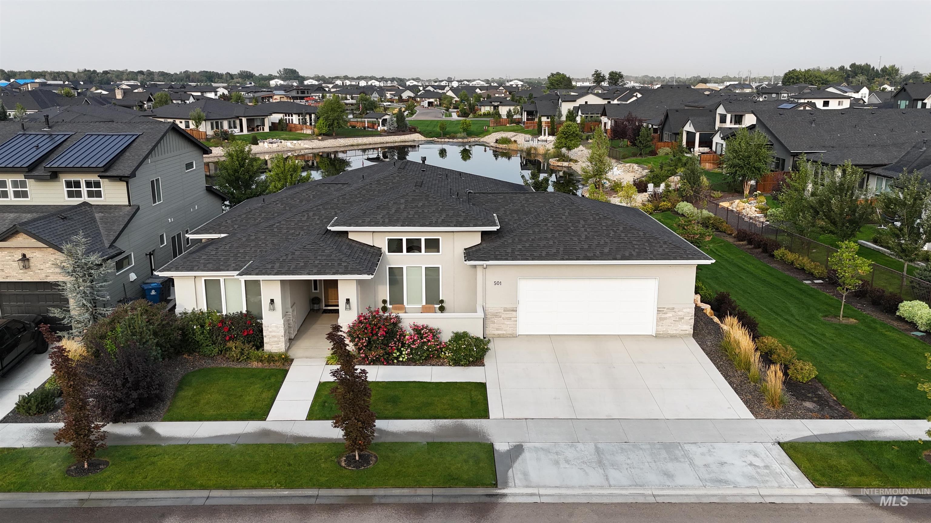 View of front of home with a residential view, stucco siding, roof with shingles, driveway, and stone siding