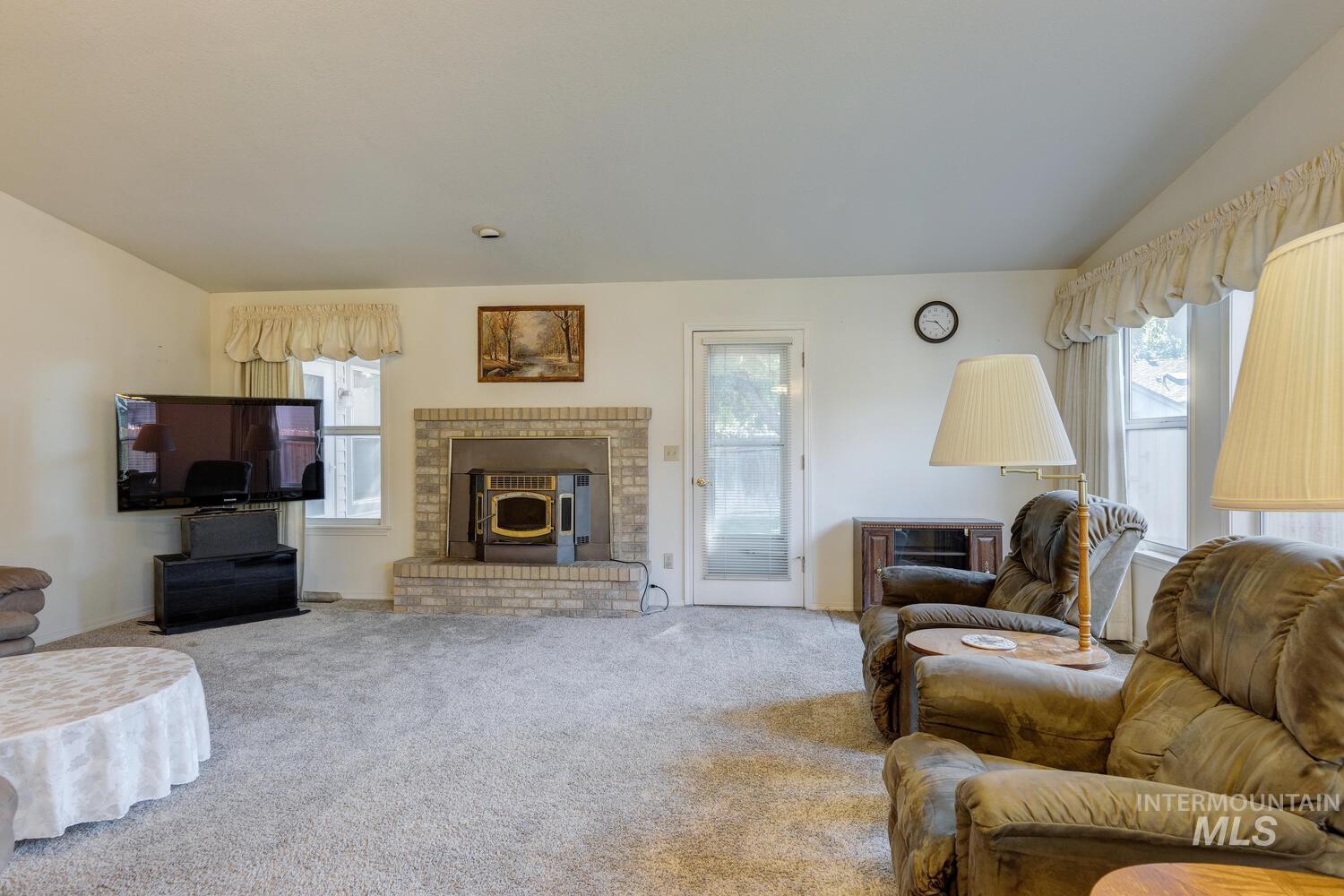 Carpeted living area featuring lofted ceiling and a wood stove