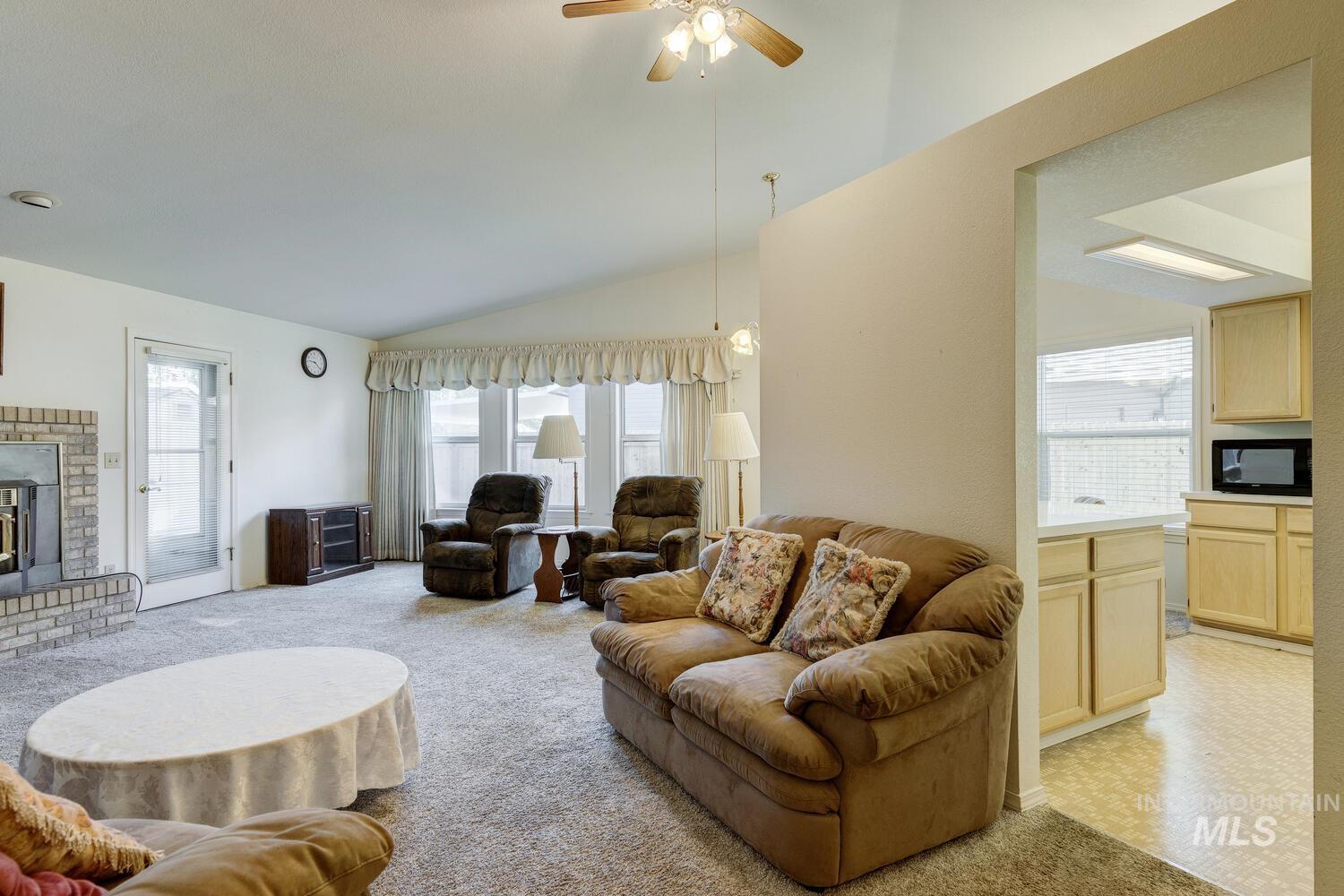 Living room with vaulted ceiling, a brick fireplace, a ceiling fan, and light colored carpet