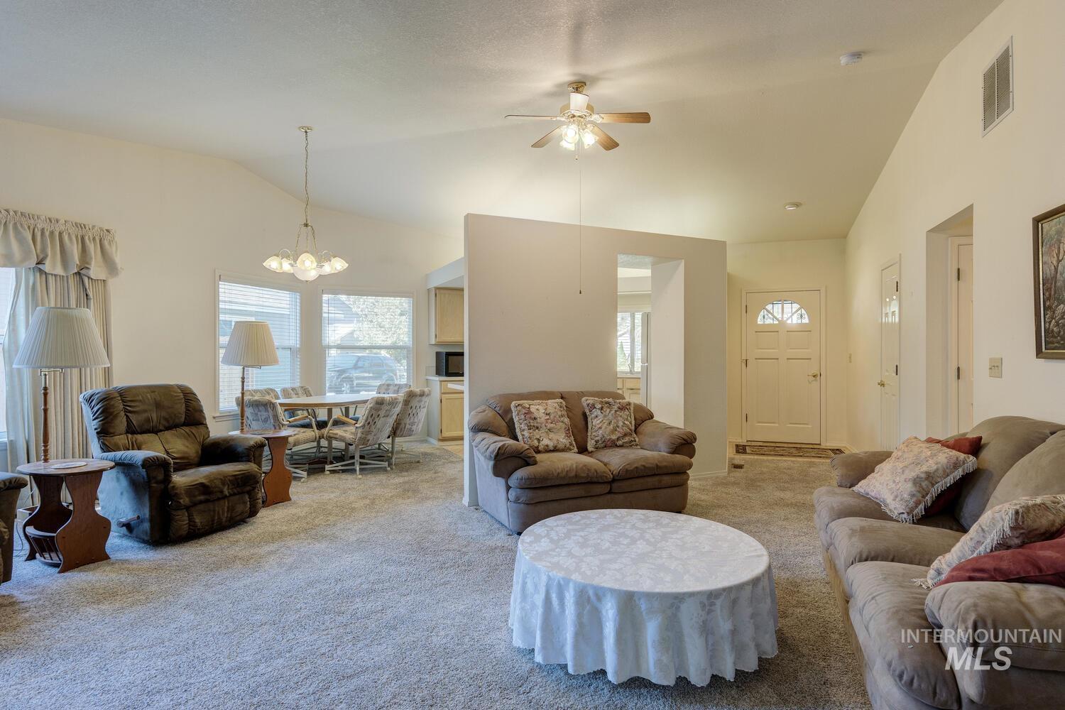 Carpeted living area featuring ceiling fan, high vaulted ceiling, and a chandelier