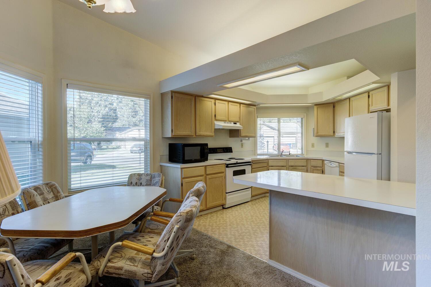Kitchen featuring light brown cabinets, white appliances, light countertops, a raised ceiling, and light colored carpet