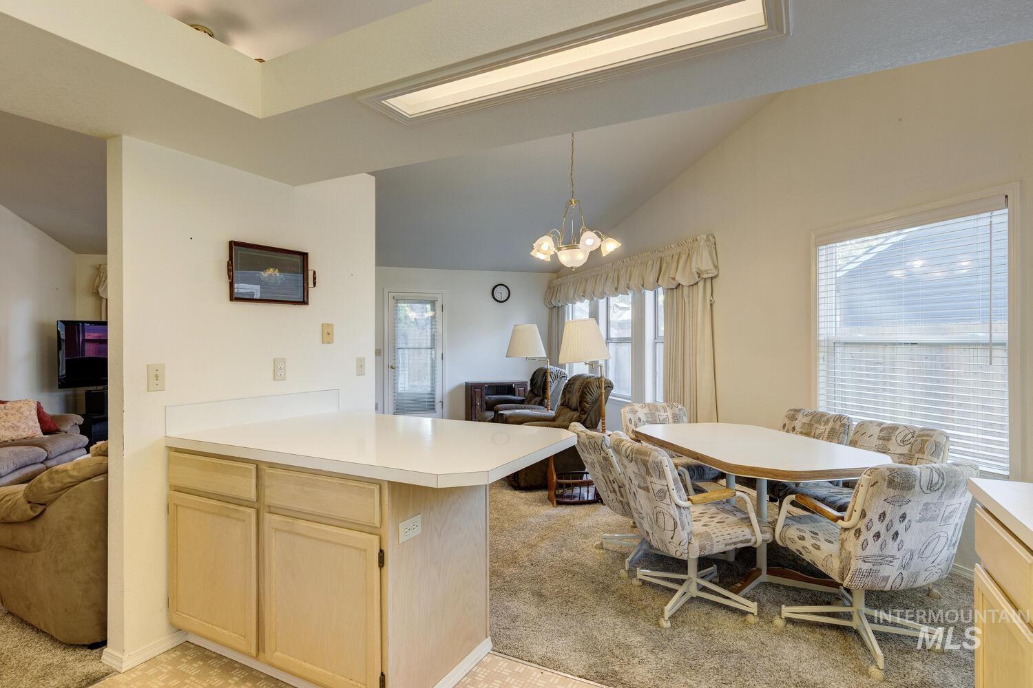 Kitchen featuring light brown cabinetry, open floor plan, light colored carpet, light countertops, and vaulted ceiling