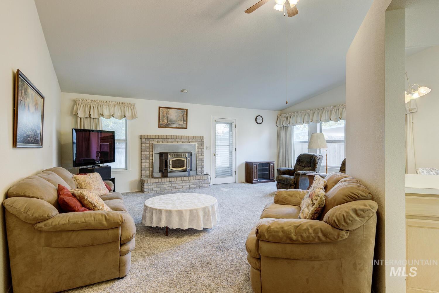 Carpeted living area with lofted ceiling, ceiling fan, plenty of natural light, and a wood stove