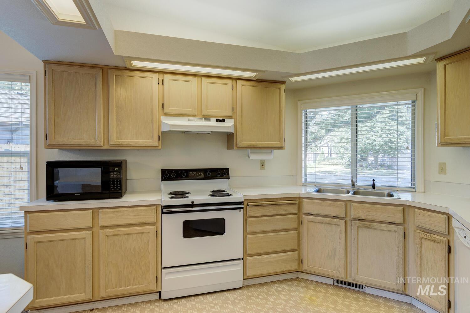 Kitchen with light brown cabinetry, white appliances, light countertops, and under cabinet range hood