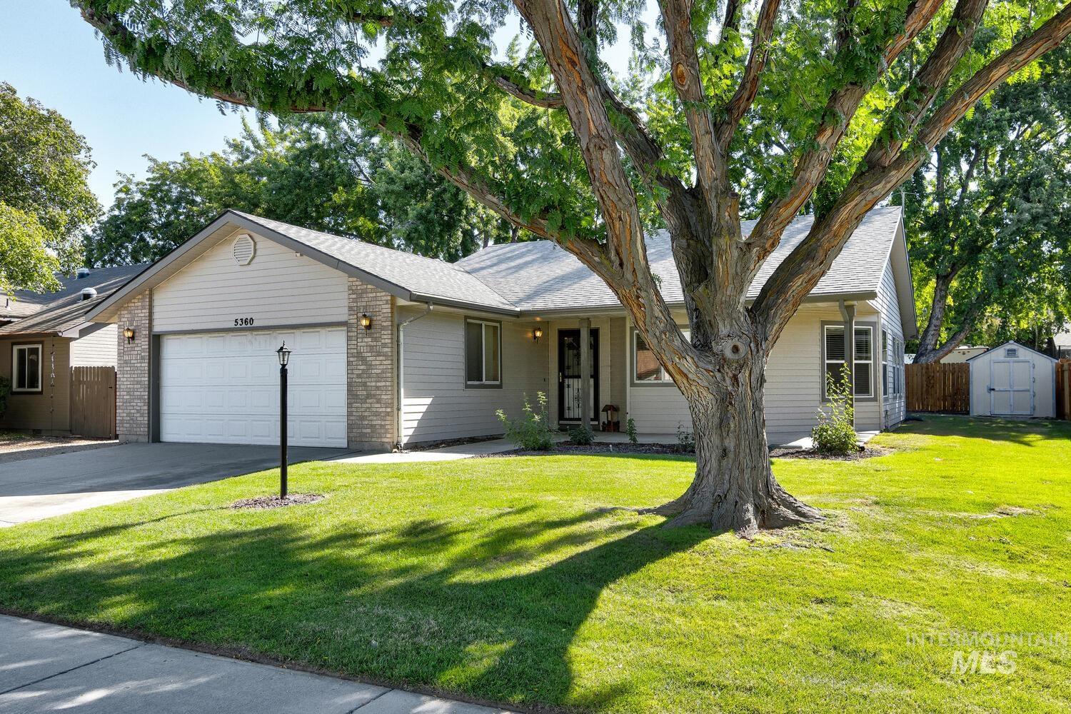 View of front of home featuring an attached garage, brick siding, concrete driveway, a storage unit, and a shingled roof