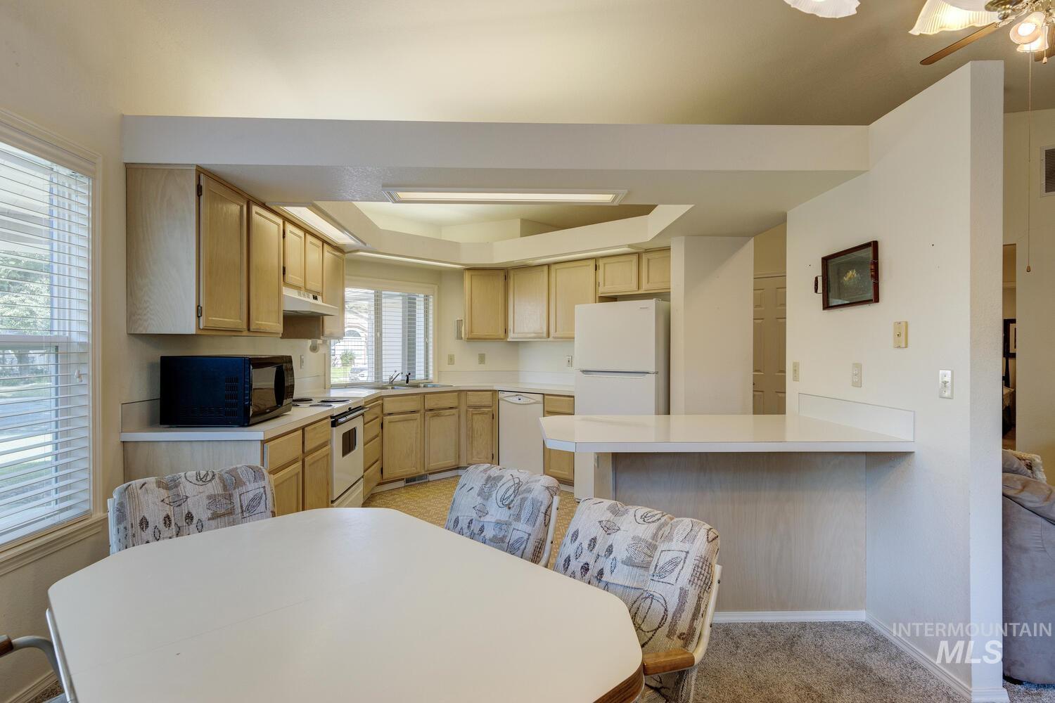 Kitchen featuring light brown cabinets, light countertops, white appliances, a peninsula, and a tray ceiling