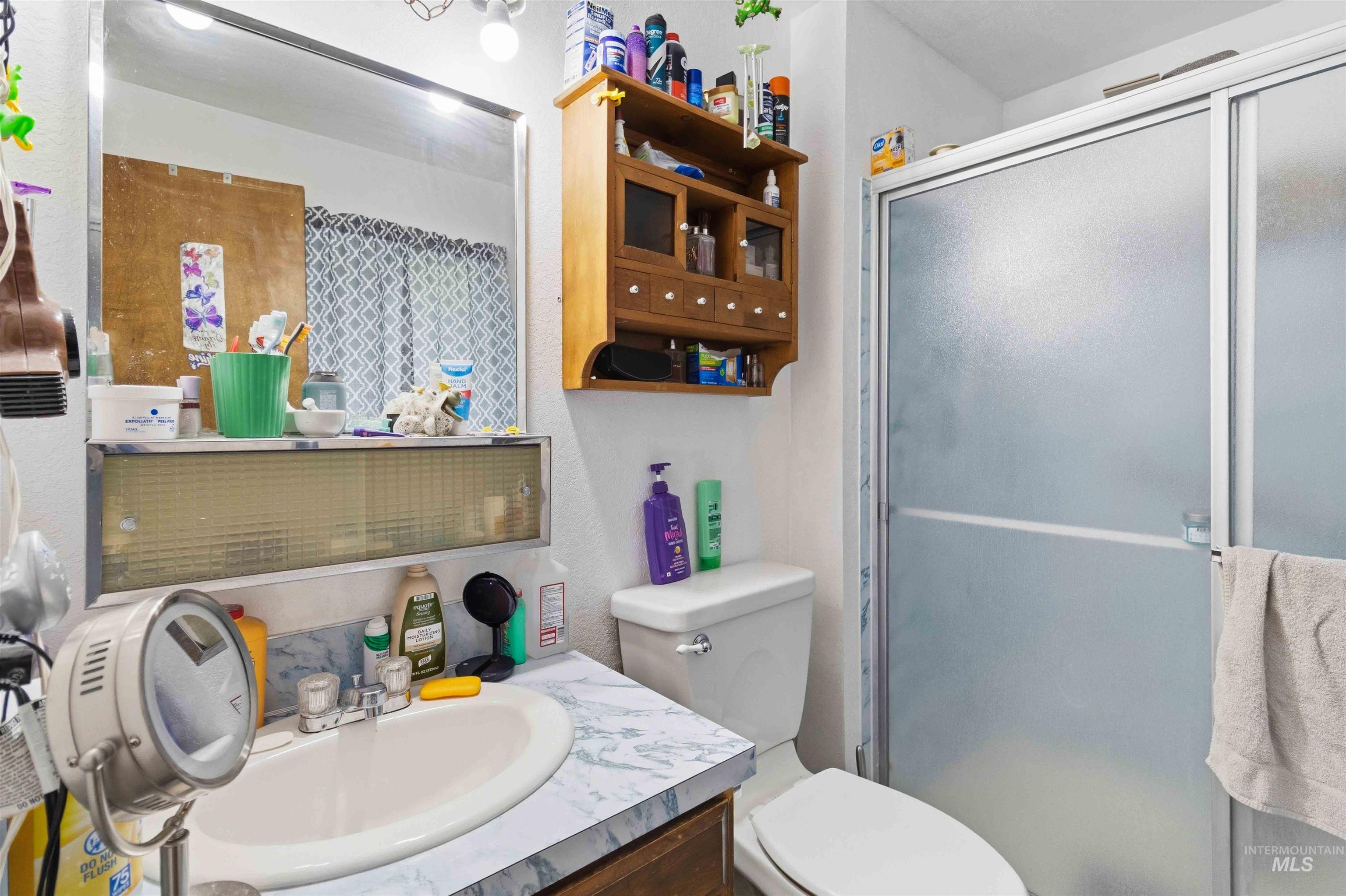 Bathroom featuring a single vanity with an oval sink, a wall-mounted medicine cabinet, and a shower with frosted glass doors