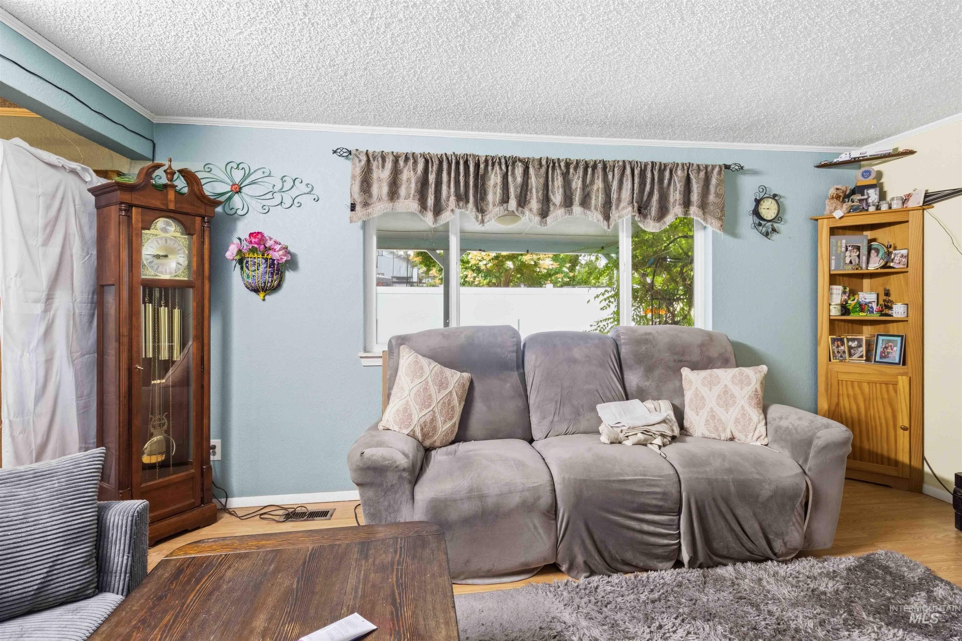 Living area featuring wood-finish flooring, a white-framed window, and crown molding