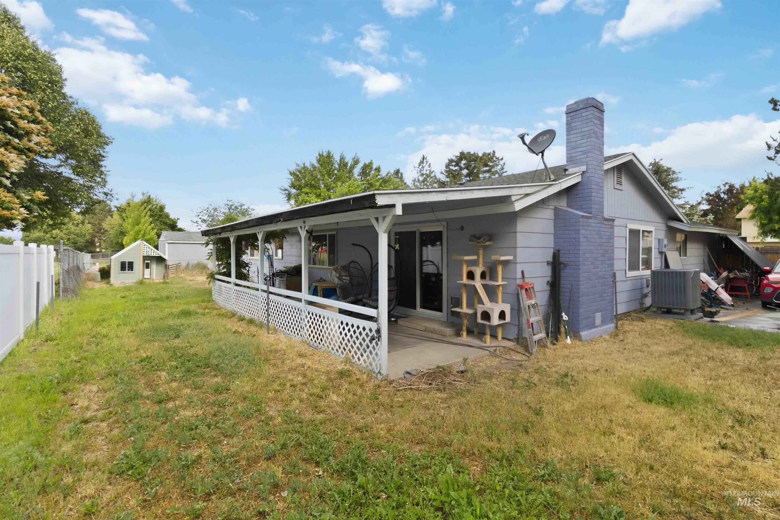 Rear exterior featuring a covered patio with white lattice railing, sliding glass door, and a brick chimney