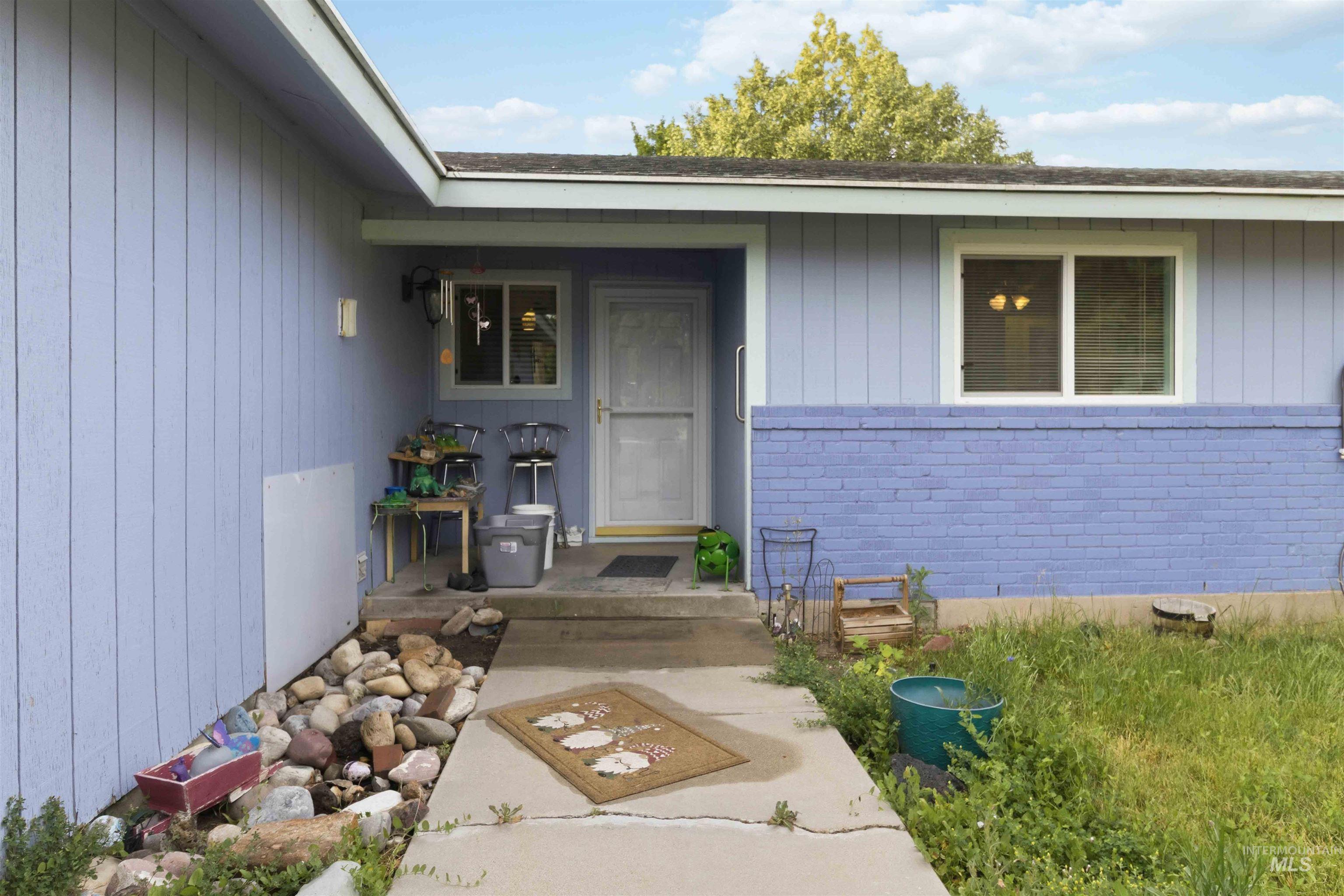 Exterior entry featuring a concrete pathway, a painted brick facade, light blue siding, a white front door, and white frame windows