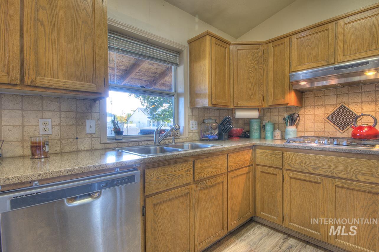 Kitchen with appliances with stainless steel finishes, brown cabinets, tasteful backsplash, under cabinet range hood, and vaulted ceiling