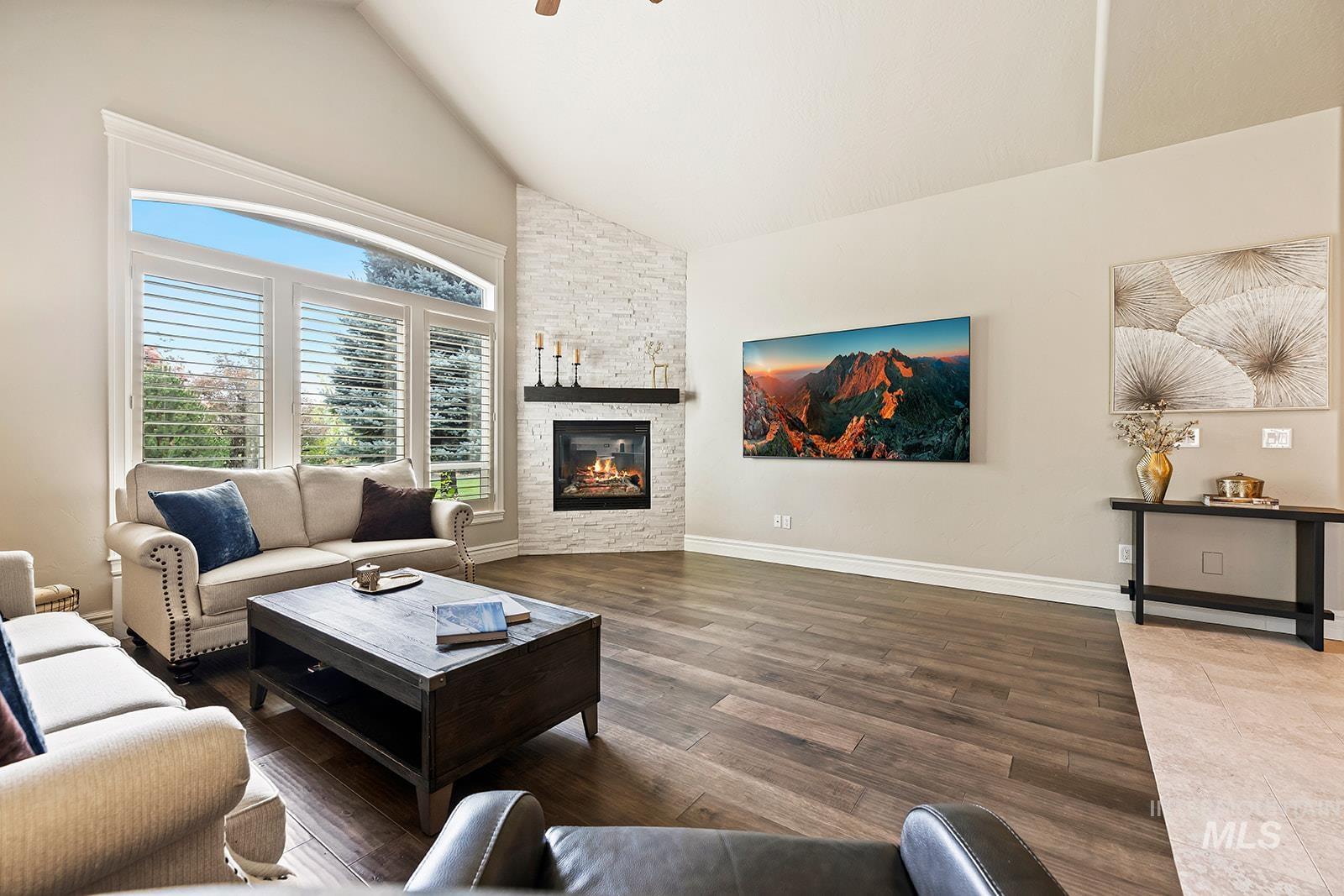 Living area with high vaulted ceiling, wood finished floors, and a stone fireplace