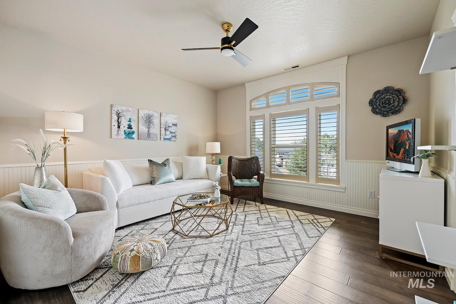 Living room with a wainscoted wall, wood finished floors, a ceiling fan, and a textured ceiling
