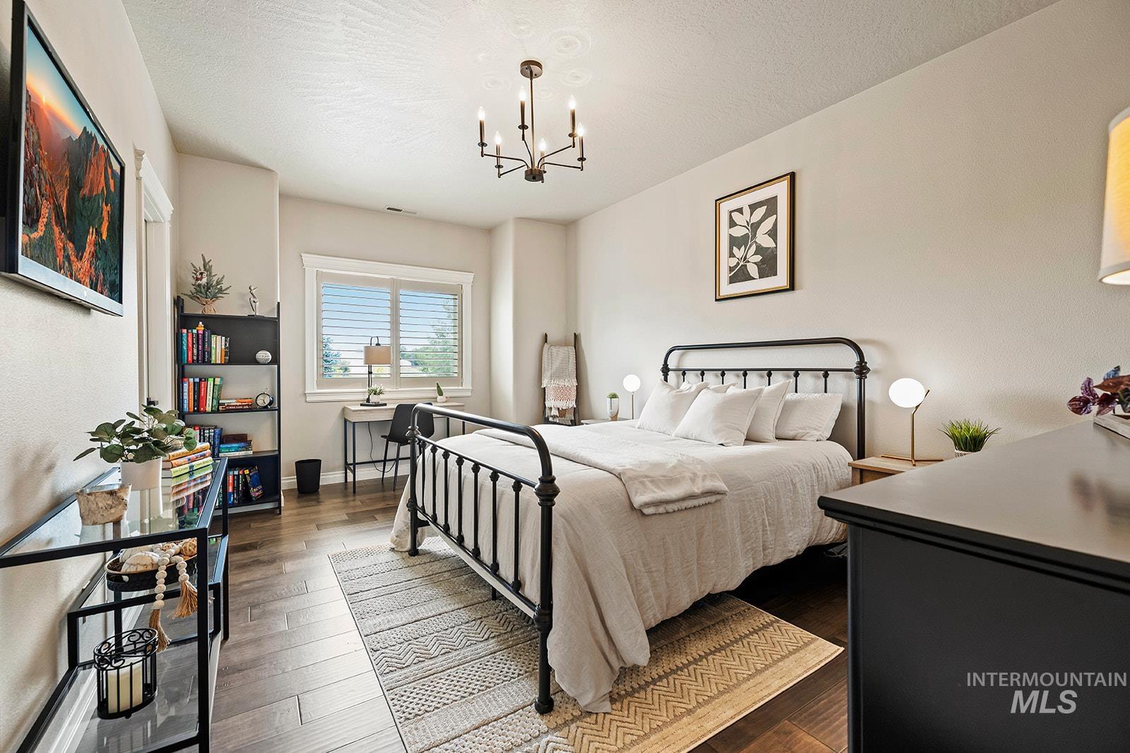 Bedroom with dark wood-style flooring, a chandelier, and a textured ceiling