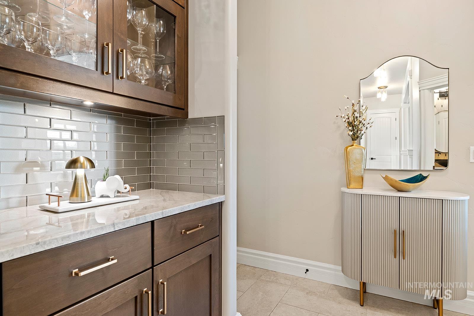 Bar area with glass insert cabinets, light stone counters, dark brown cabinetry, tasteful backsplash, and light tile patterned flooring