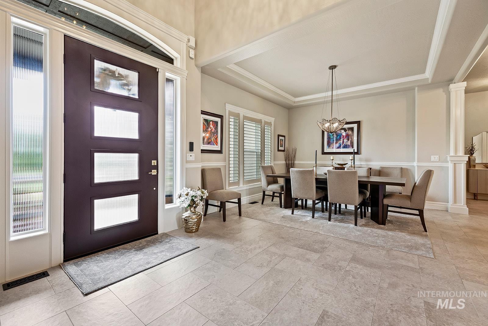 Foyer featuring a raised ceiling, a chandelier, and ornate columns