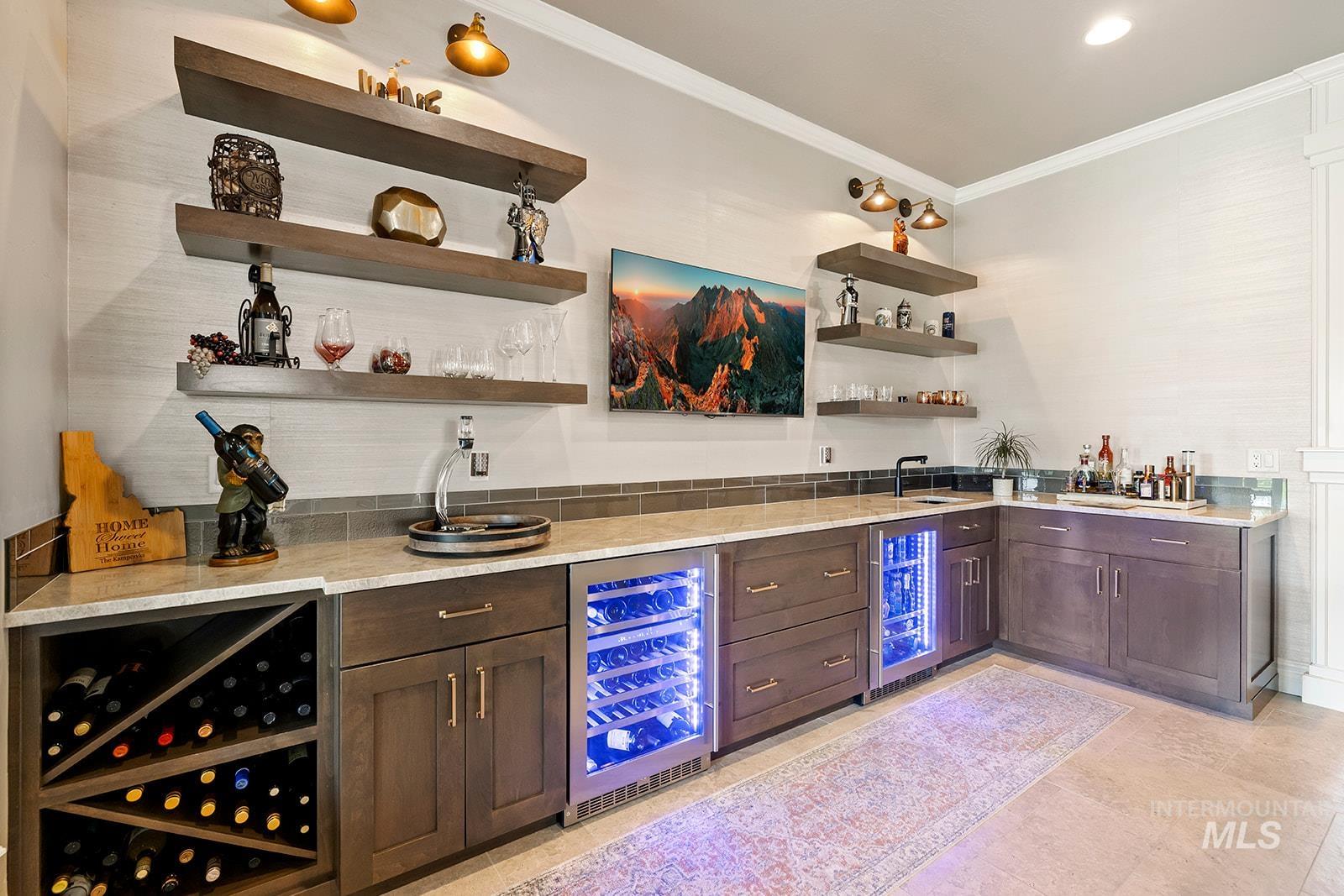 Indoor wet bar featuring open shelves, dark brown cabinetry, beverage cooler, and crown molding