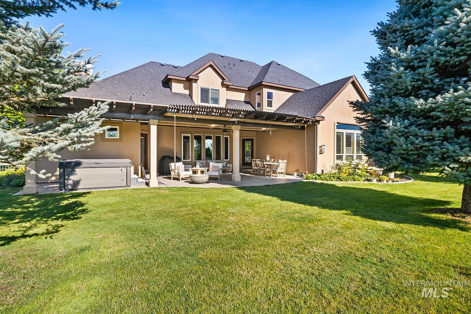 Back of property featuring a hot tub, stucco siding, a patio, and a lawn