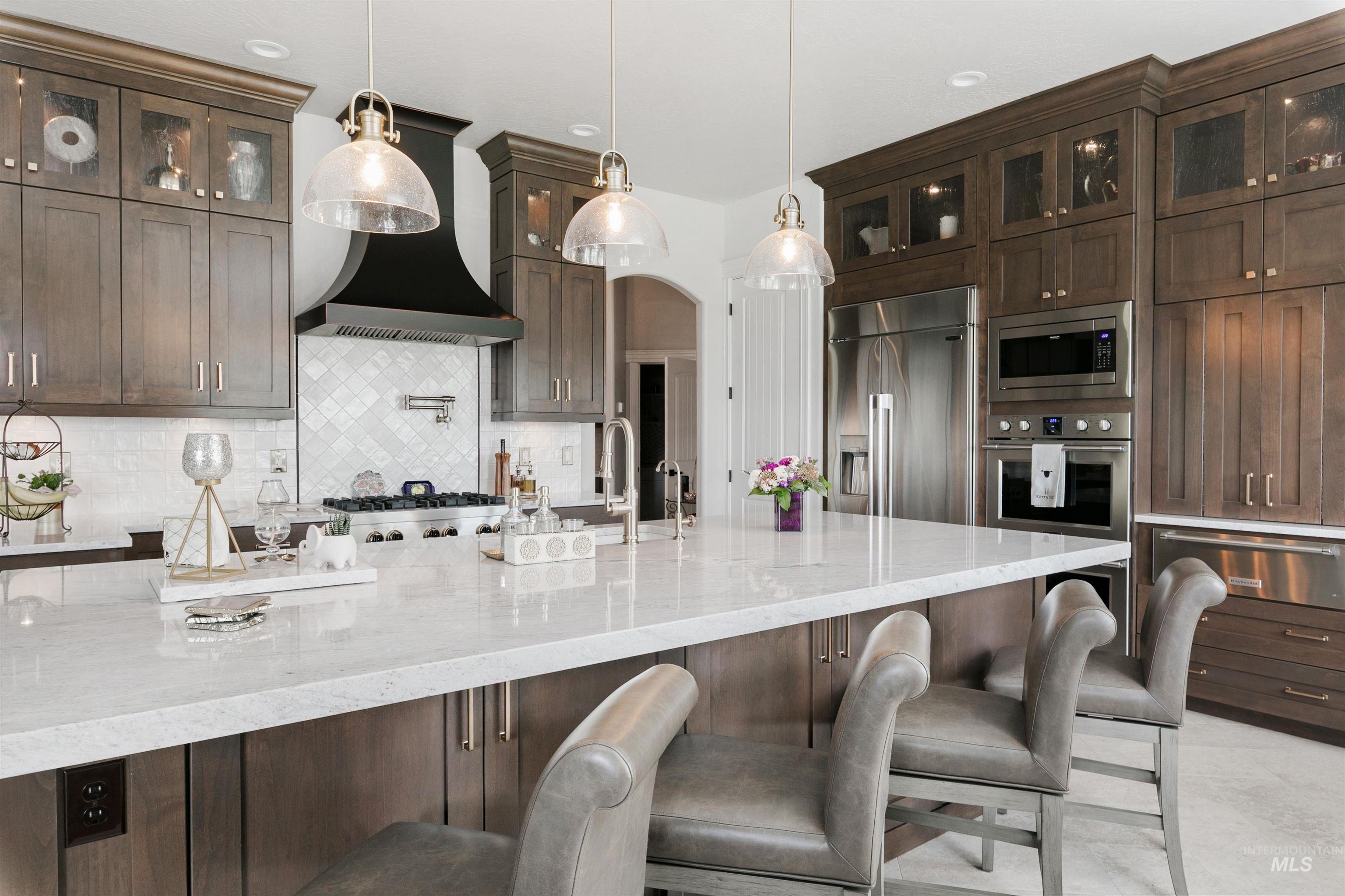 Kitchen featuring dark brown cabinetry, light stone counters, arched walkways, glass insert cabinets, and decorative backsplash