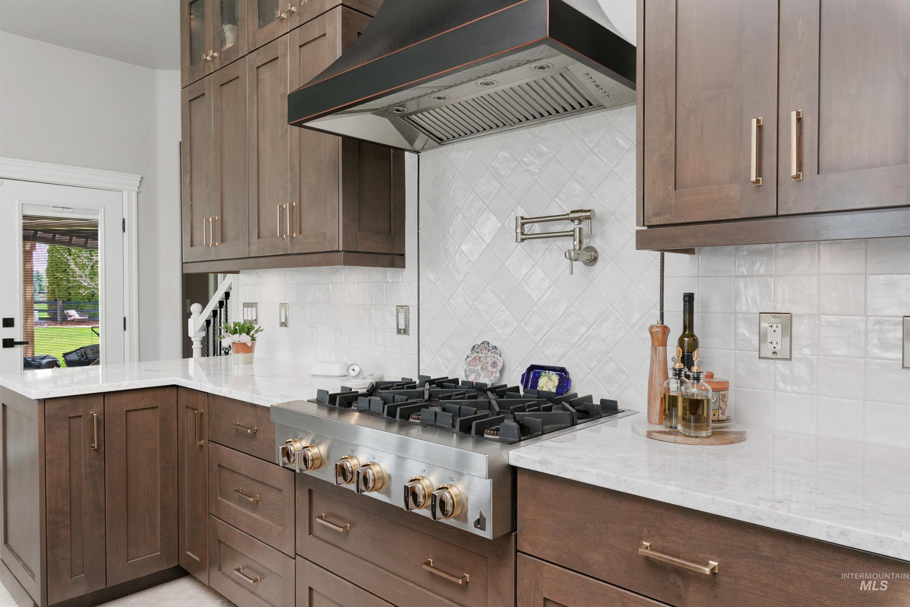 Kitchen featuring custom range hood, light stone counters, stainless steel gas cooktop, and dark brown cabinetry