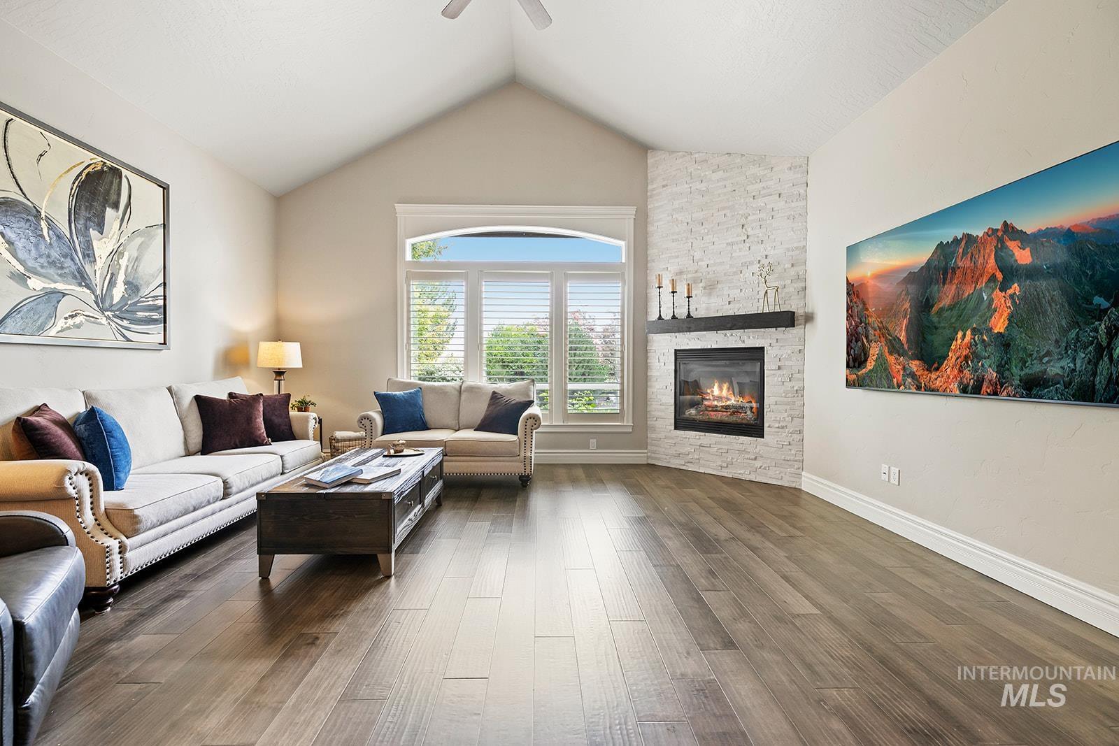 Living area featuring dark wood-type flooring, lofted ceiling, a stone fireplace, and ceiling fan