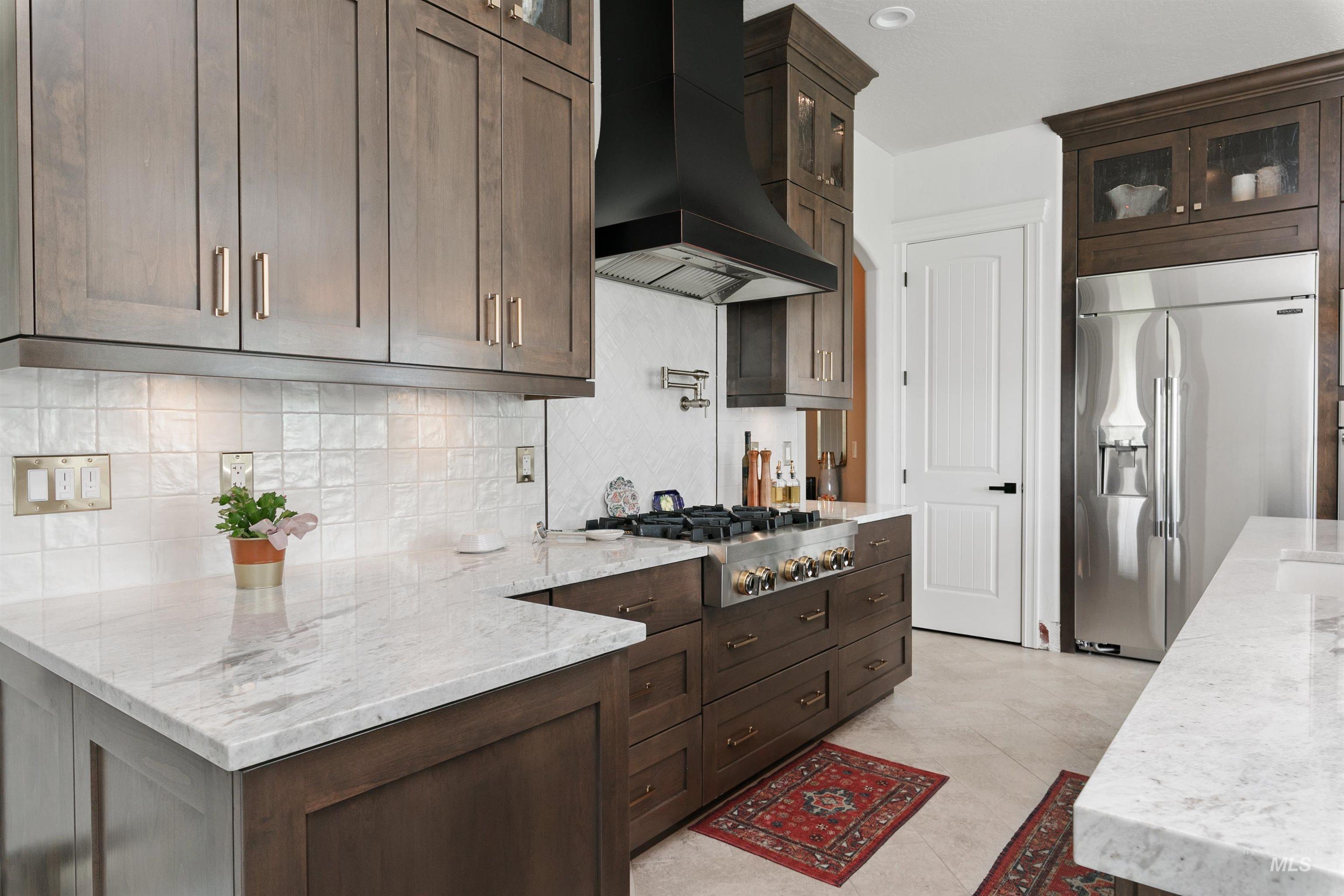 Kitchen featuring dark brown cabinets, light stone counters, glass insert cabinets, and appliances with stainless steel finishes