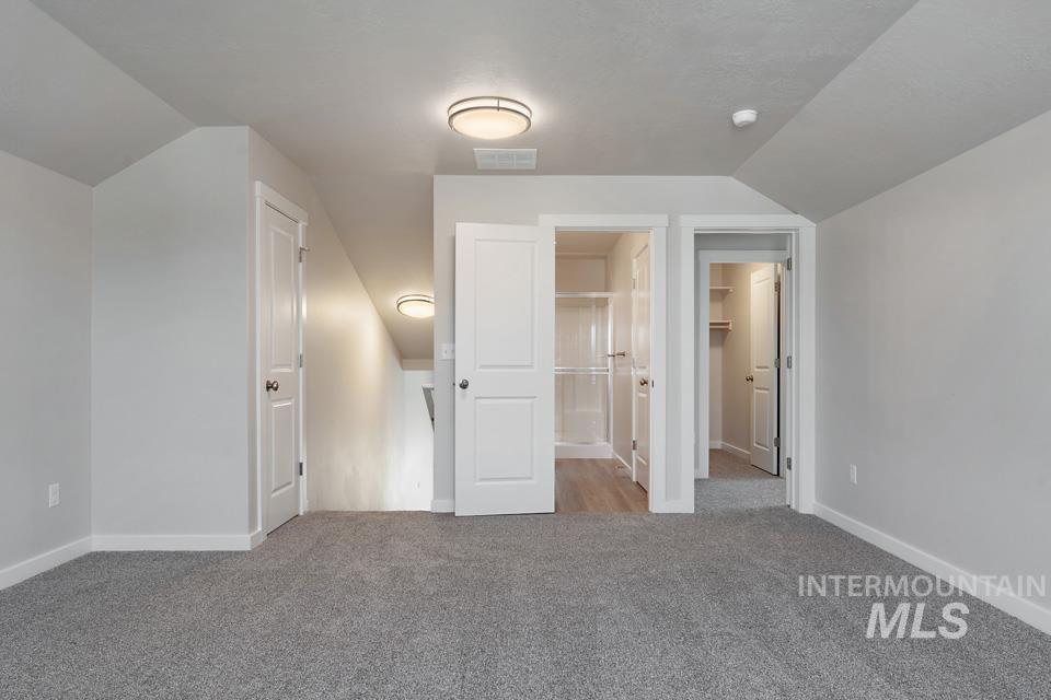 Unfurnished bedroom featuring light carpet, lofted ceiling, and a walk in closet