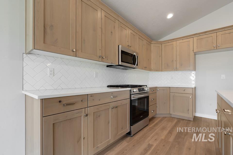 Kitchen with appliances with stainless steel finishes, light brown cabinetry, vaulted ceiling, light countertops, and light wood-type flooring