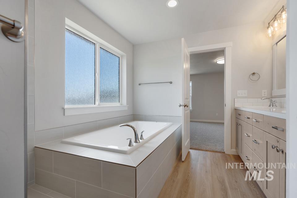 Bathroom featuring vanity, a bath, and wood finished floors