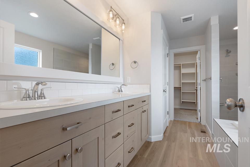 Bathroom with double vanity, wood finished floors, a spacious closet, tasteful backsplash, and a tile shower