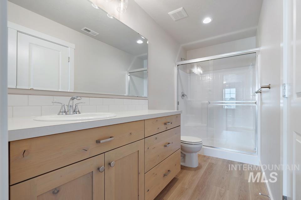 Bathroom featuring vanity, wood finished floors, a shower stall, decorative backsplash, and recessed lighting